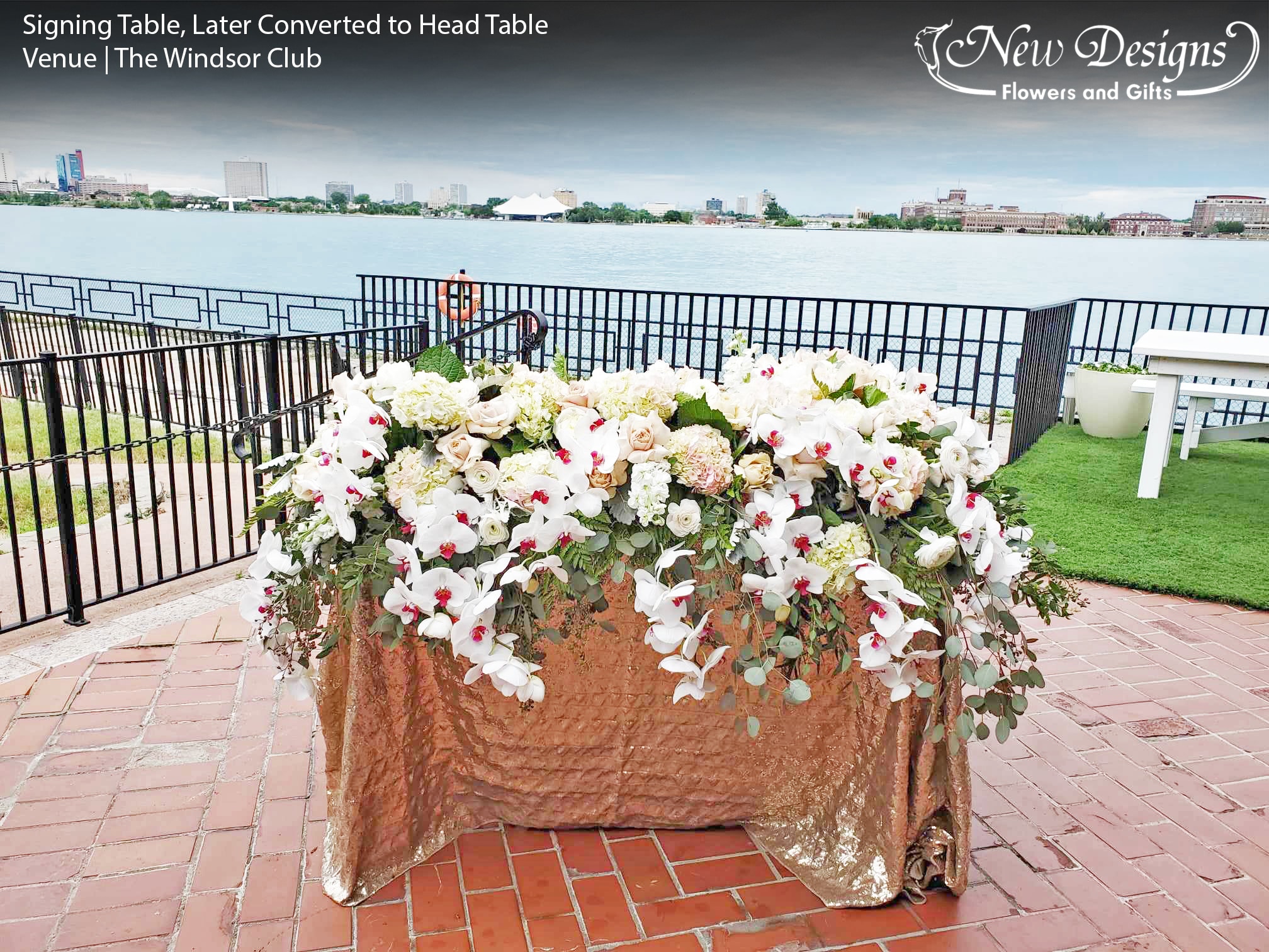 A Signing Table, at an outdoor venue along the water, with a Gold Sequined table cloth, overflowing with Roses and Phalaenopsis Orchids